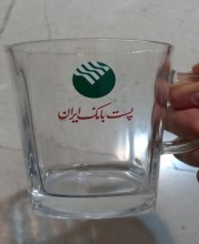 لیبل UV DTF چسبیده شده روی لیوان که رویش آرم پست بانک ایران چاپ شده